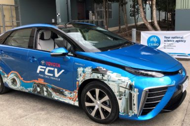 A bright blue Toyota Mirai which is a fuel cell vehicle that runs on hydrogen parked in front of a CSIRO banner