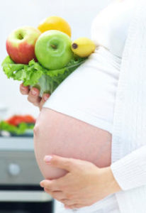 Pregnant person holding a bowl of fruit and veg.